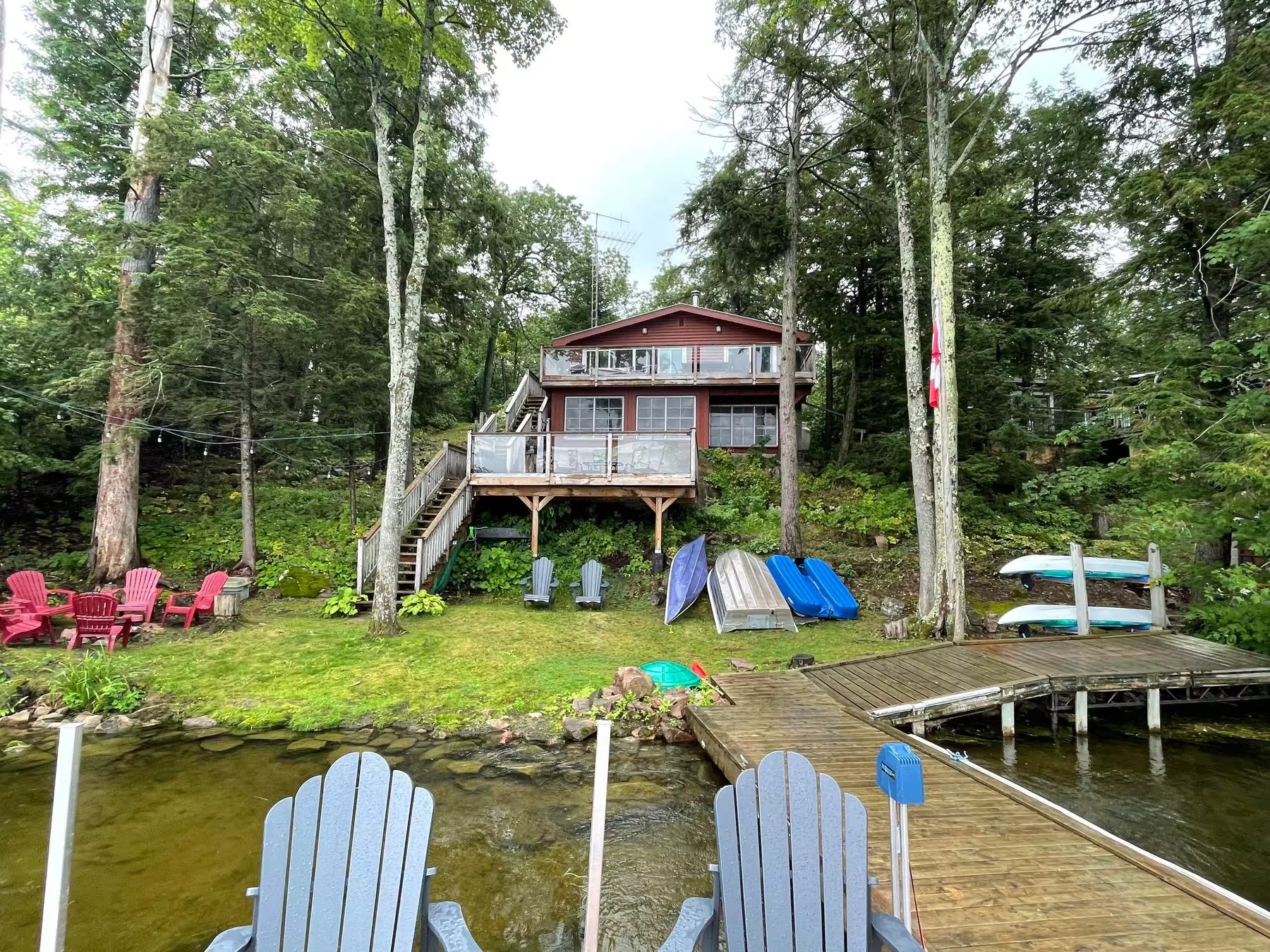 Jacob’s Lakehouse seen from the dock in summer, with the decks, stairs and boats on the lawn